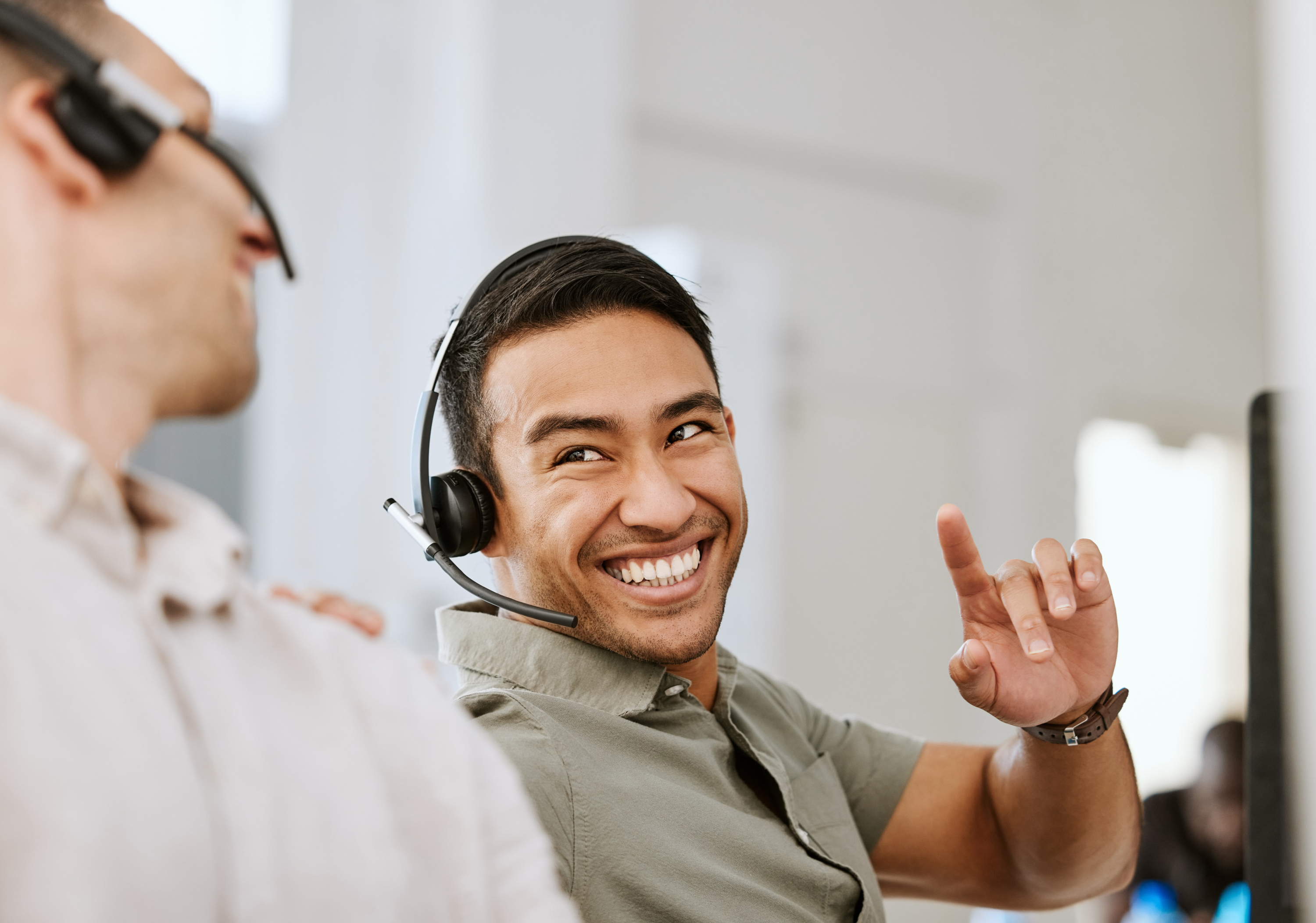 Two men wearing headsets with microphones are laughing and pointing at each other.