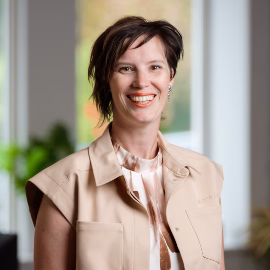 An employee is standing in an office setting for a professional headshot or team photo.