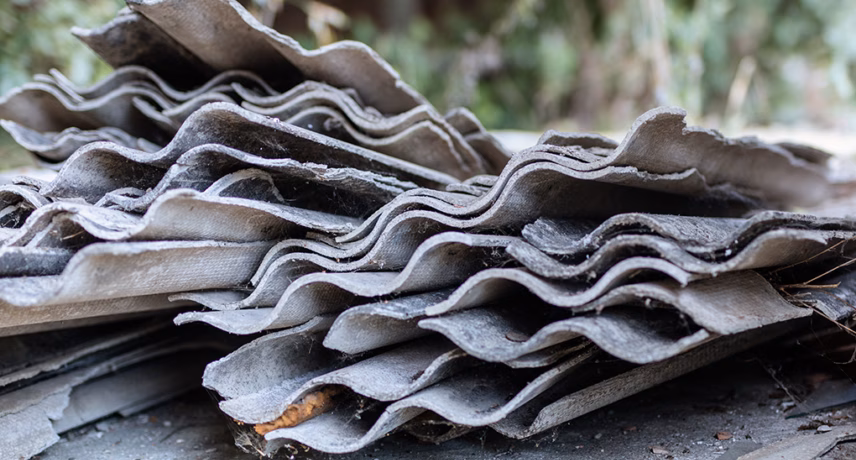 Stacked corrugated sheets made of asbestos-containing material, stored for disposal or processing.