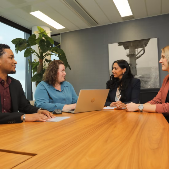 Four employees discuss their work and collaboration during a meeting in a modern conference room.