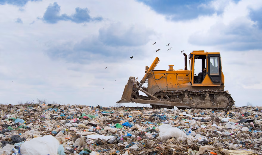 A bulldozer moves and processes waste at a landfill as part of waste management.