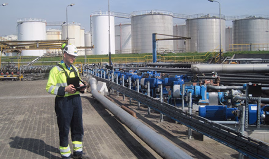 An employee checks equipment and pipes during a visual inspection at an industrial site.