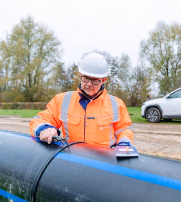 An employee is inspecting a pipe using specialized measuring equipment during an on-site inspection.