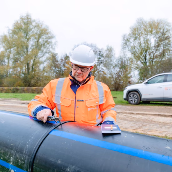 An employee is inspecting a pipe using specialized measuring equipment during an on-site inspection.