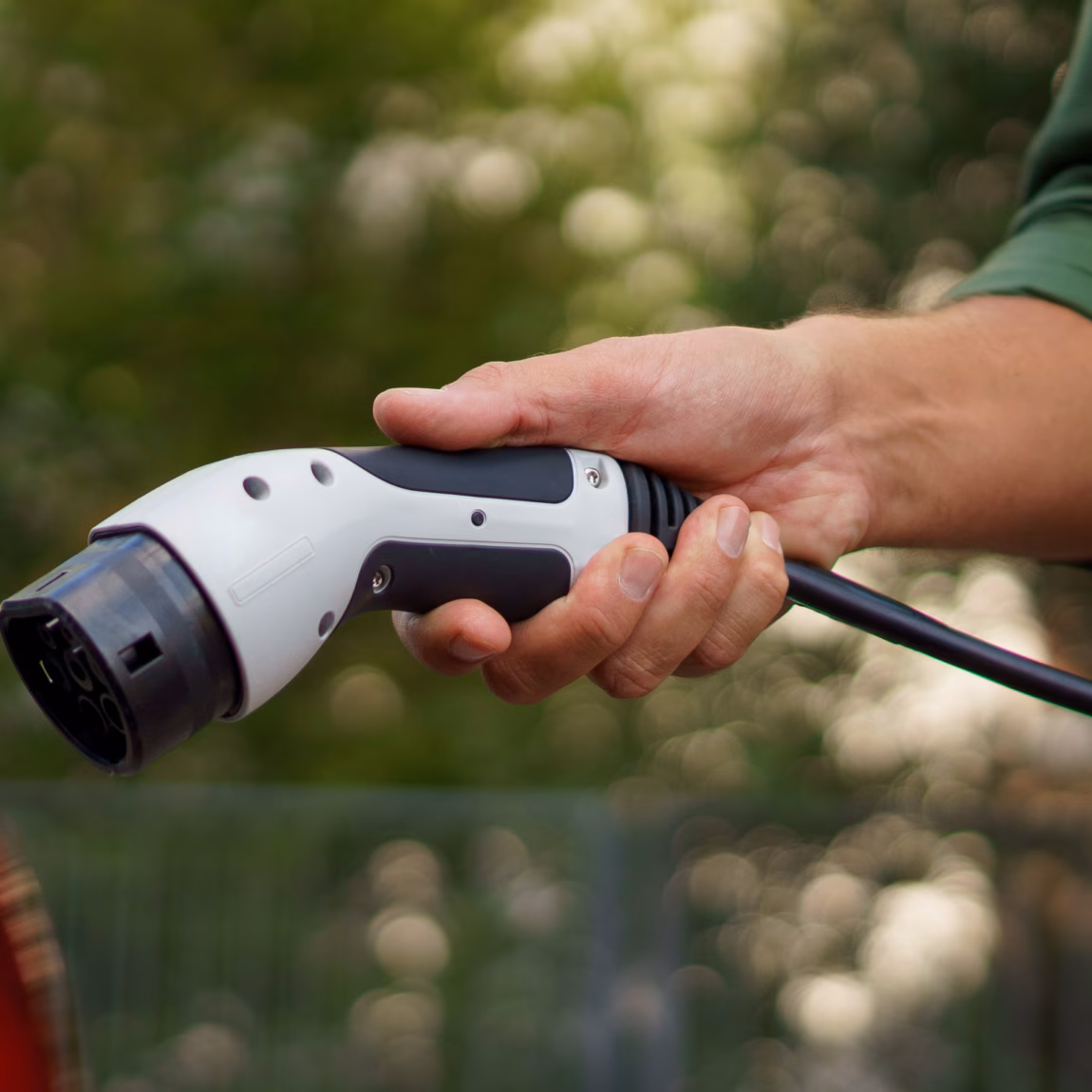A man holding power supply cable at electric vehicle charging station, closeup