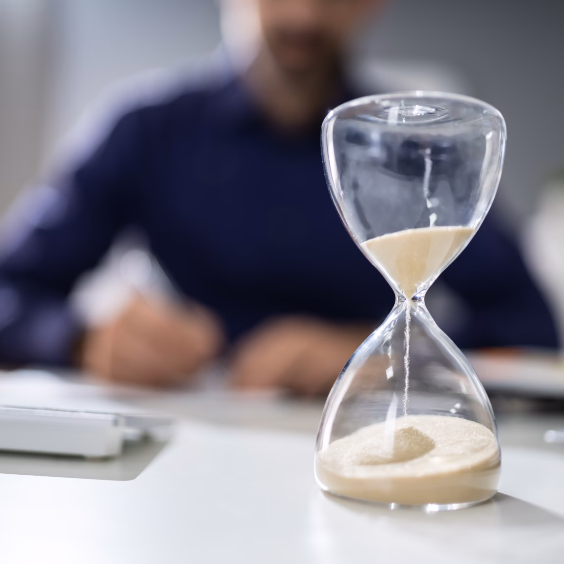 Close-up Of Hourglass In Front Of Businessperson's Hand Calculating Invoice