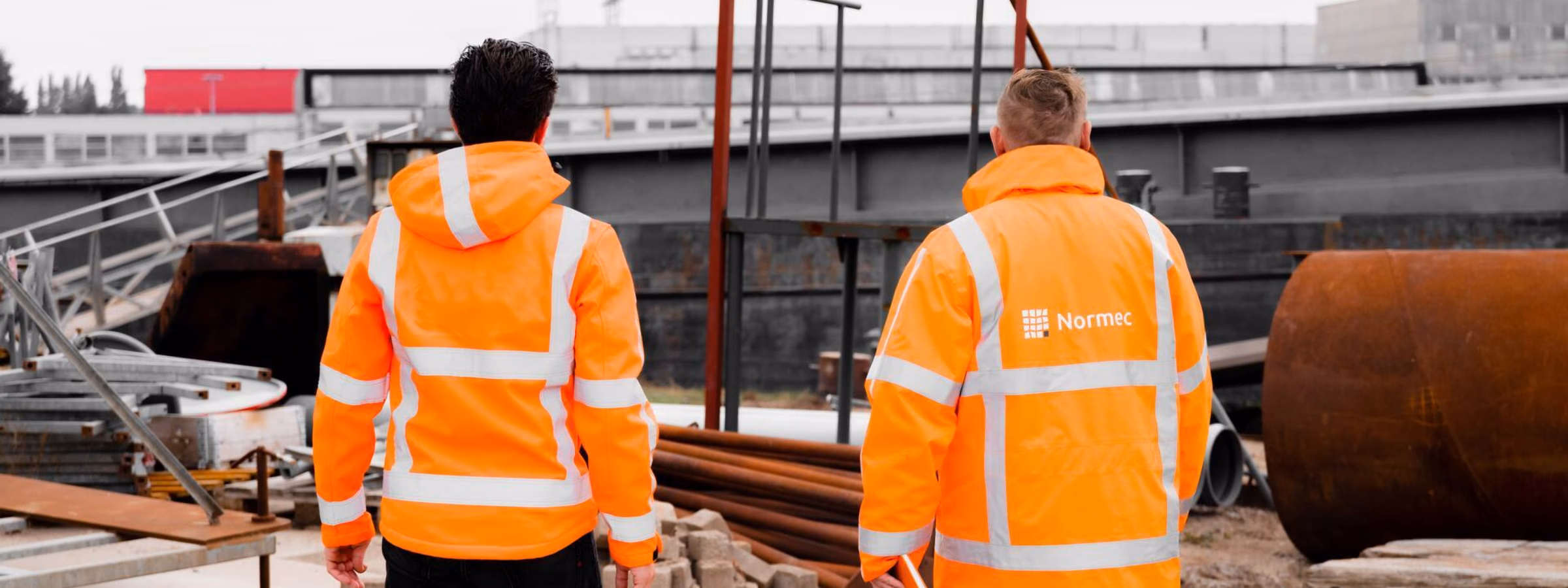 Zwei Mitarbeiter in reflektierender Sicherheitskleidung führen eine Standortbegehung auf einer Industriebaustelle durch.