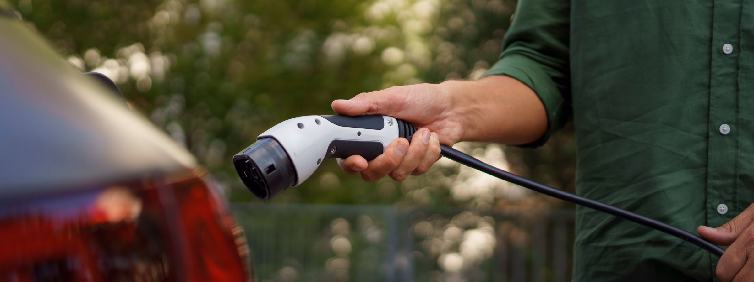 A man holding power supply cable at electric vehicle charging station, closeup