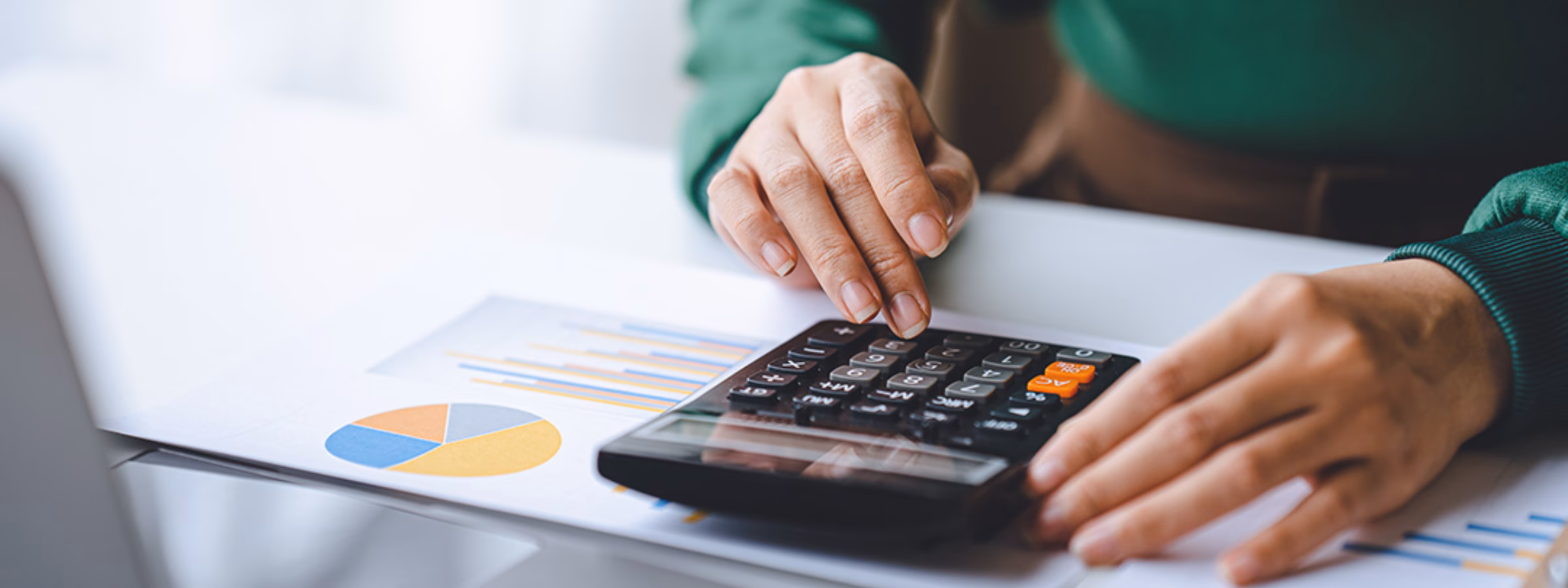Eine Person nutzt einen Taschenrechner, um Finanzdaten zu analysieren, neben Diagrammen und einem Laptop.