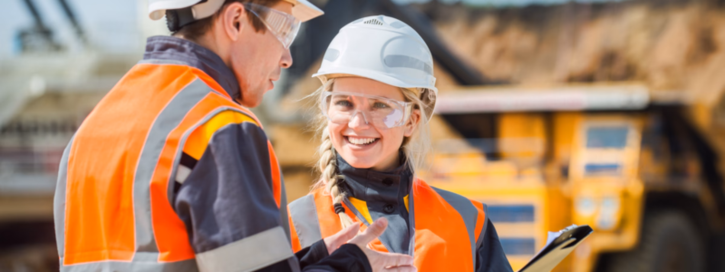 Zwei Mitarbeiter in reflektierender Sicherheitskleidung und mit Schutzhelmen besprechen Inspektionsdaten auf einer industriellen Baustelle.
