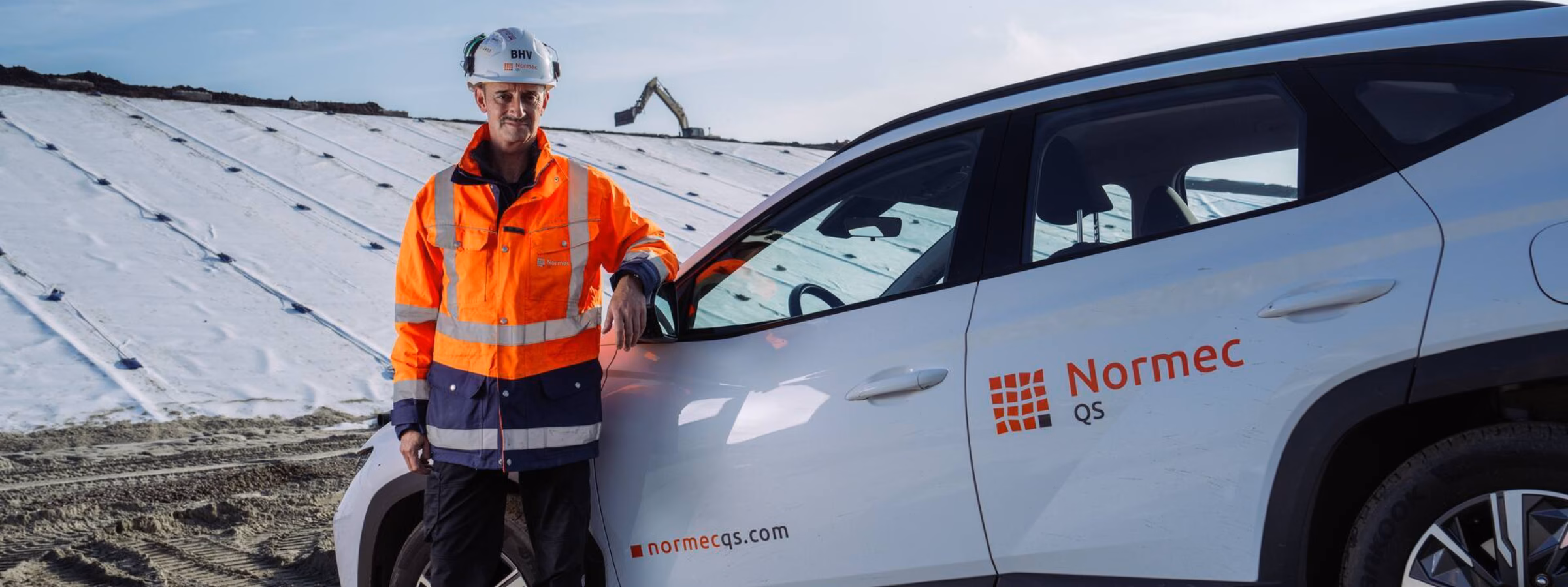 Een inspecteur staat bij een dienstvoertuig op locatie voor inspectie- en controlewerkzaamheden.