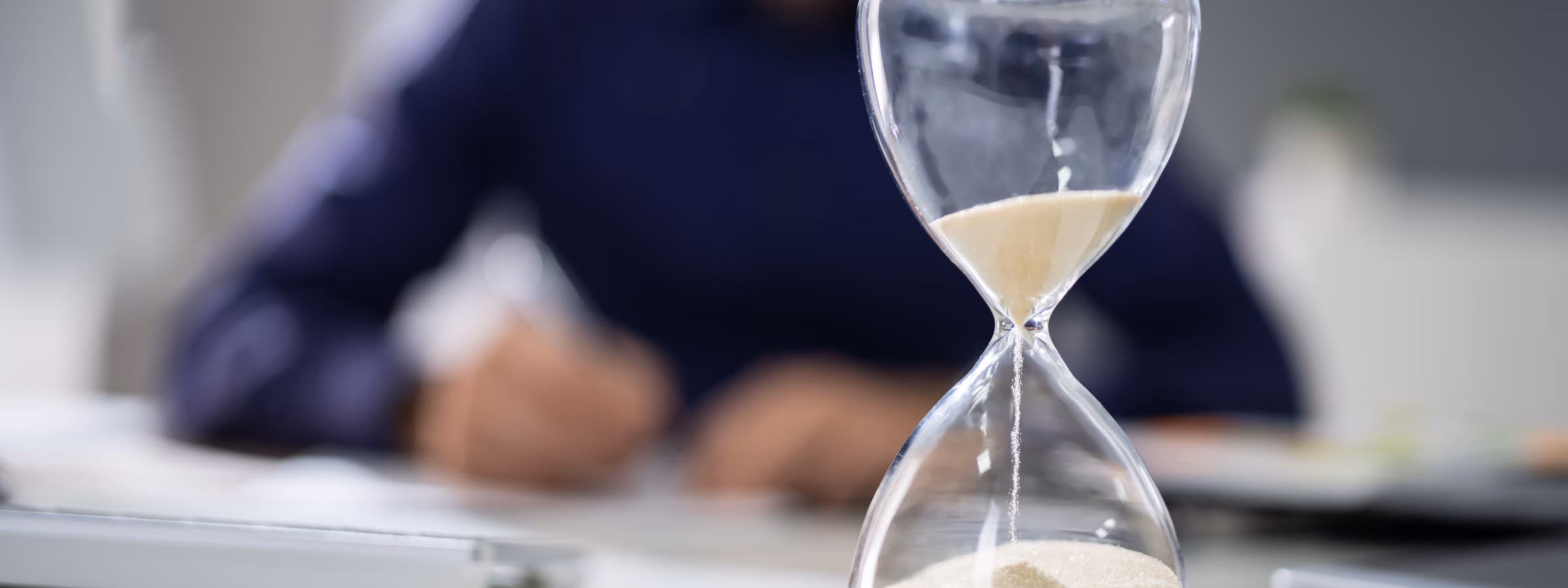Close-up Of Hourglass In Front Of Businessperson's Hand Calculating Invoice