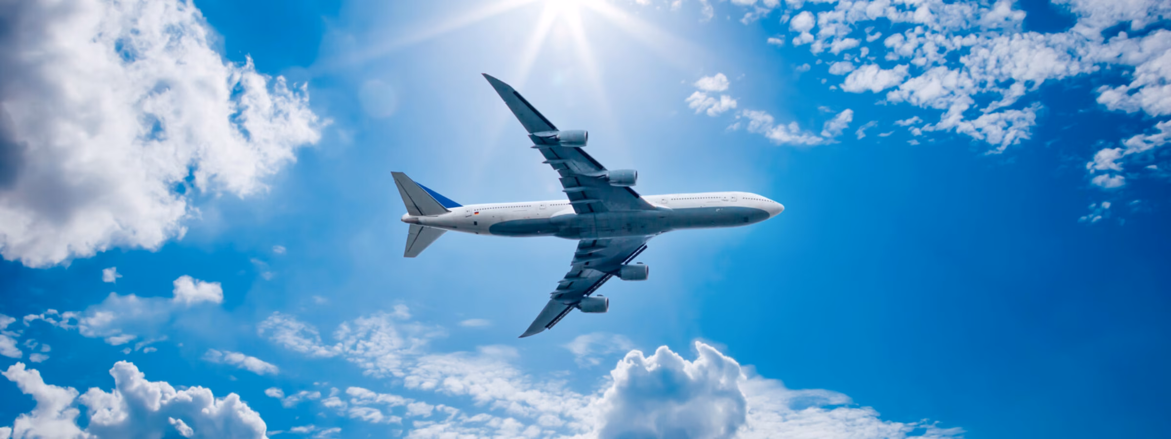 A passenger plane is flying at cruising altitude beneath a clear sky with clouds.