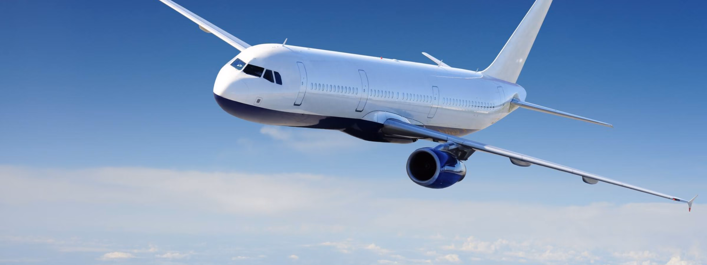 A passenger plane is flying at cruising altitude above a layer of clouds.