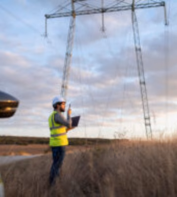 Een medewerker voert een inspectie uit bij een hoogspanningslijn in een landelijke omgeving.