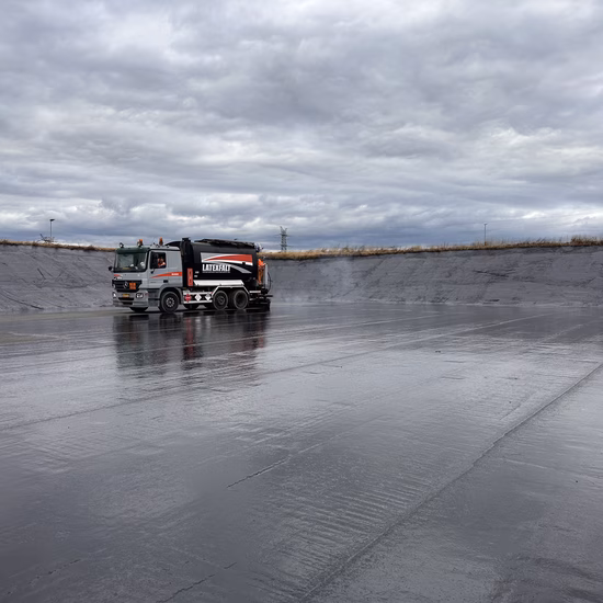 Voertuig voert werkzaamheden uit op een grote waterdichte folieconstructie onder een bewolkte lucht.