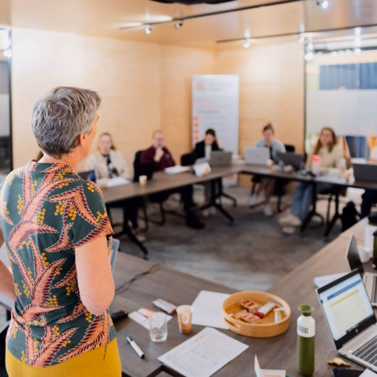 Schulung oder Workshop mit Teilnehmern an einem Konferenztisch, während ein Referent in einem modernen Schulungsraum eine Präsentation hält.