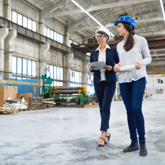 Two people wearing safety helmets are inspecting an industrial production facility and discussing construction or production plans.
