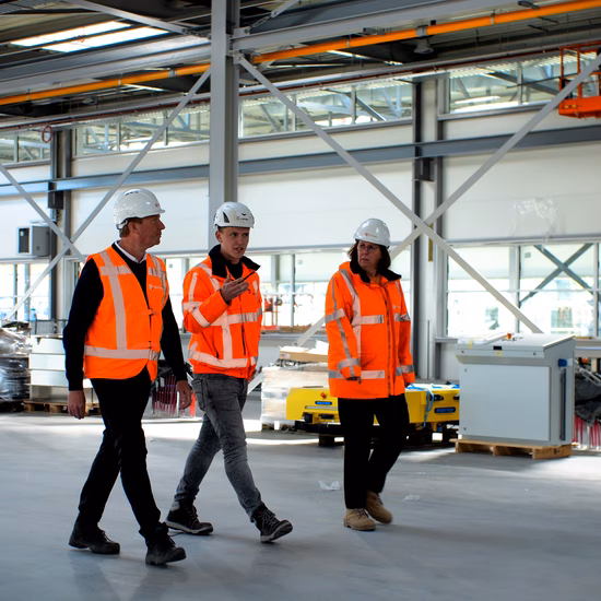 Mitarbeiter in Schutzkleidung gehen während einer Inspektion oder eines Rundgangs durch eine industrielle Produktionshalle.
