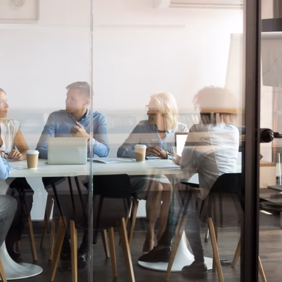 A group of employees in discussion at a conference table in a modern office space.