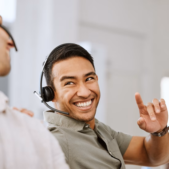 Mitarbeiter mit Headsets beraten sich während des Kundenkontakts an einem Büroarbeitsplatz.