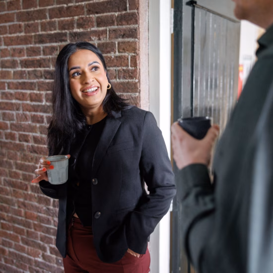 Two people talking near an entrance with a brick wall, while one person is holding a drink.