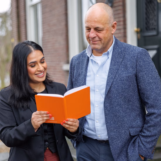 Two professionals are discussing information in a notebook during a conversation outside a building.