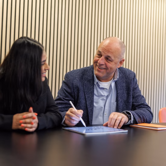 Two colleagues are reviewing notes during a meeting at a conference table.