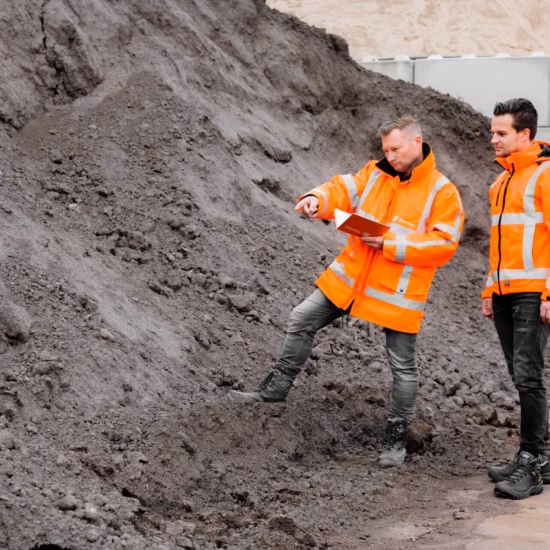 Two employees in safety gear are conducting an inspection at a storage or soil processing site.