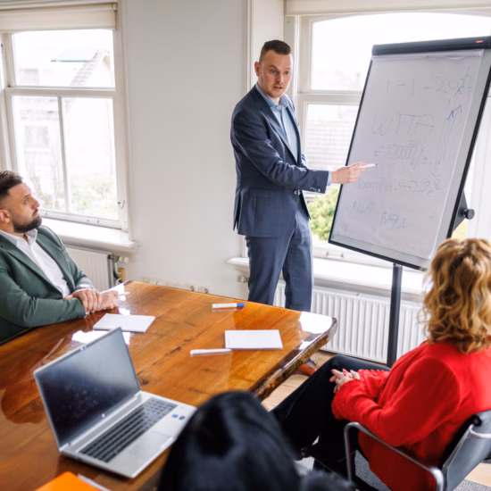 A professional is giving a presentation using a flip chart during a team meeting in a conference room.