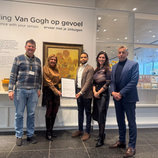 A group of employees poses with a certificate during an official recognition ceremony in a museum or visitor setting.