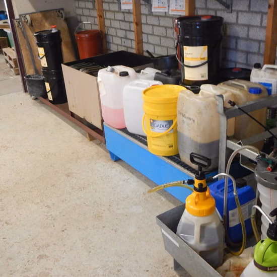Jerry cans, drums, and containers holding liquids are stored in a workshop or utility room.