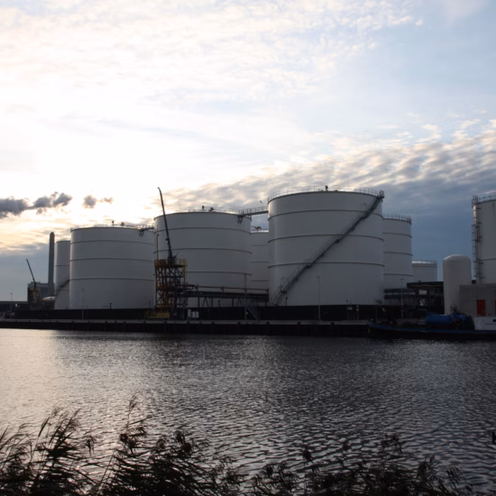 Industrial storage tanks and process facilities are located at a waterfront production site.