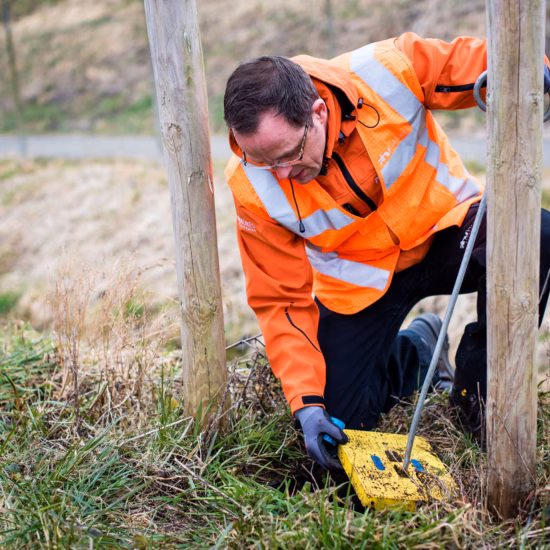 An employee is taking measurements at a monitoring well as part of on-site groundwater monitoring.