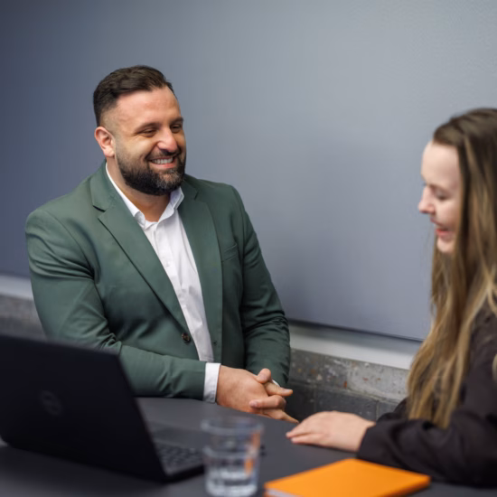 Two colleagues are talking during a meeting in a modern conference room.