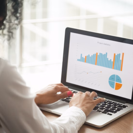 Een persoon gebruikt een laptop waarop verschillende grafieken, staafdiagrammen en een cirkeldiagram zichtbaar zijn. De afbeelding visualiseert data-analyse, rapportage, KPI-monitoring en zakelijke prestaties in een moderne werkomgeving.
