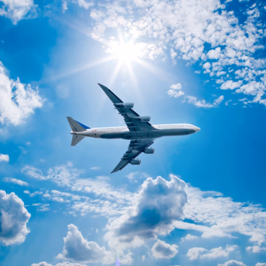 A passenger plane is flying at cruising altitude beneath a clear sky with clouds.