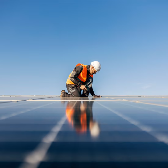 Ein technischer Mitarbeiter in Schutzkleidung führt eine Inspektion auf einem großen Solarpark durch.
