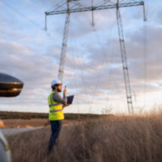 An employee is conducting an inspection of a high-voltage power line in a rural area.