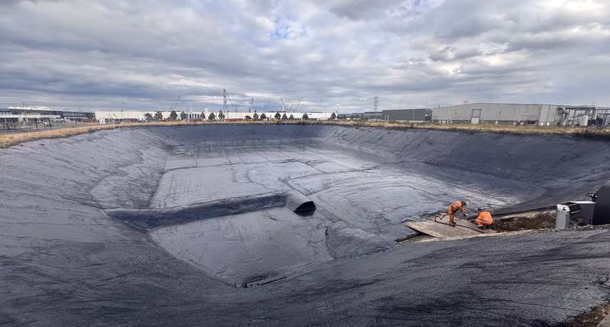 Waterdichte folie aangebracht in een groot bassin of vijver tijdens aanlegwerkzaamheden onder een bewolkte lucht.