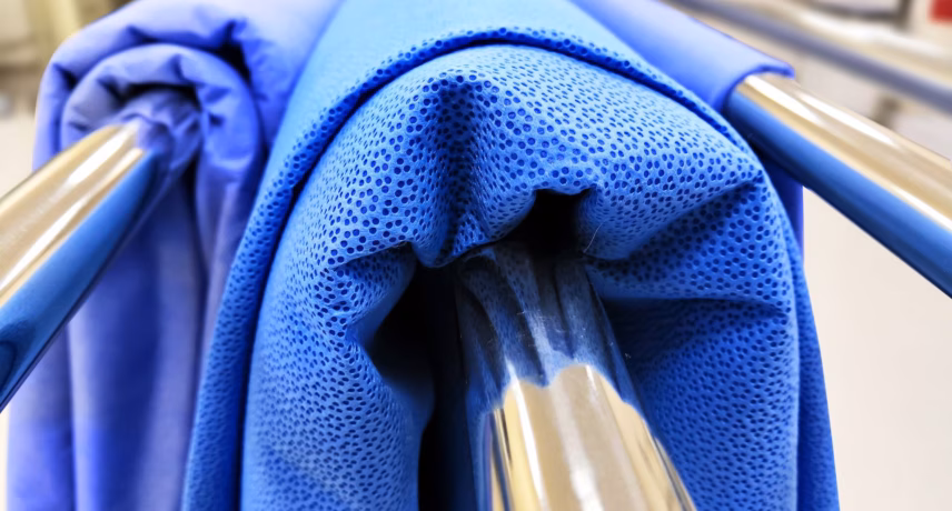 Close-up of blue technical textile material on metal rolls in an industrial setting, suitable for quality and material testing.