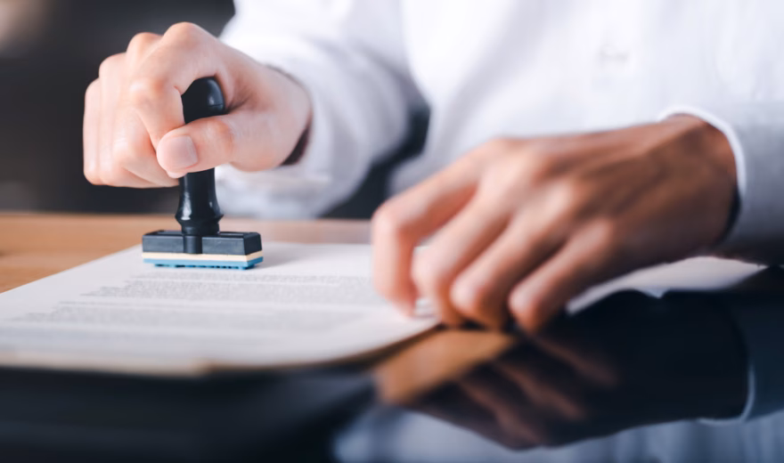 A person applies an official stamp to a document as part of a validation or approval process.