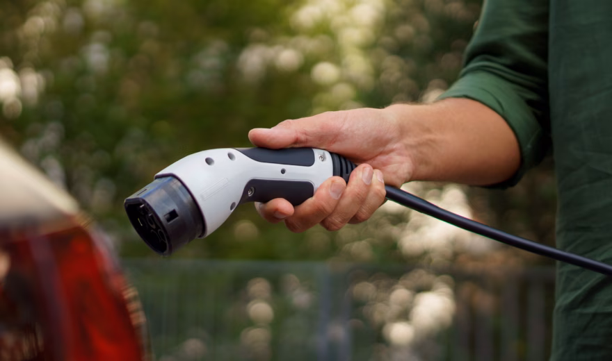 A man holding power supply cable at electric vehicle charging station, closeup
