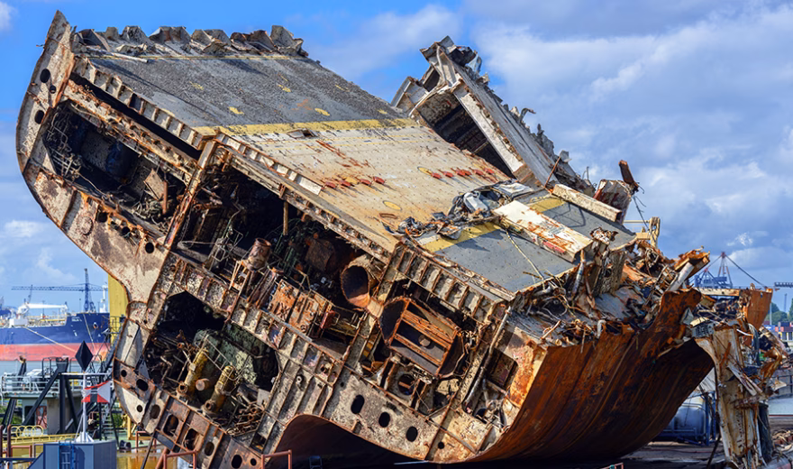 Ein stark beschädigtes und verrostetes Schiffswrack liegt auf einer Werft, um dort zerlegt und dem Recycling zugeführt zu werden.