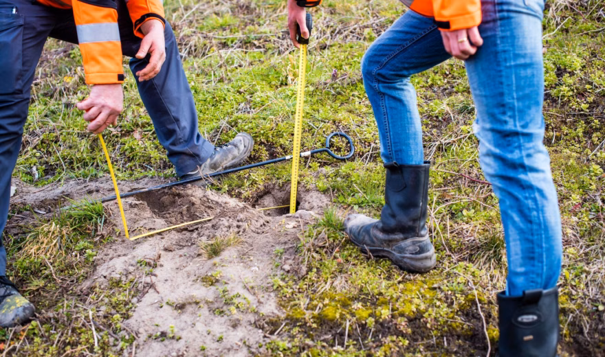 Employees perform measurements and inspection work in the field as part of a soil investigation.