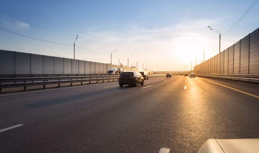 Verkeer rijdt over een snelweg met geluidswerende voorzieningen in een infrastructurele omgeving.