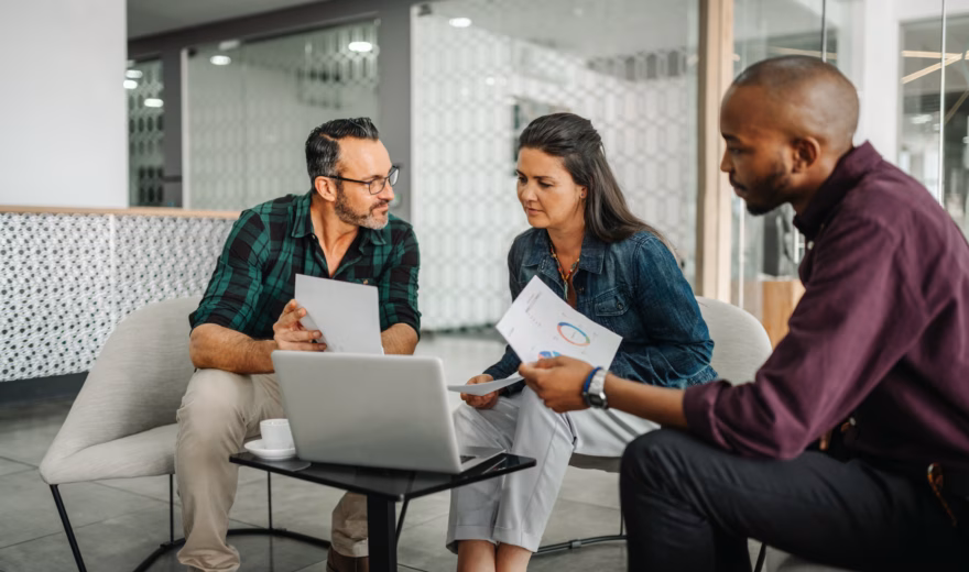 Three colleagues discuss reports and tasks during a meeting at the office.