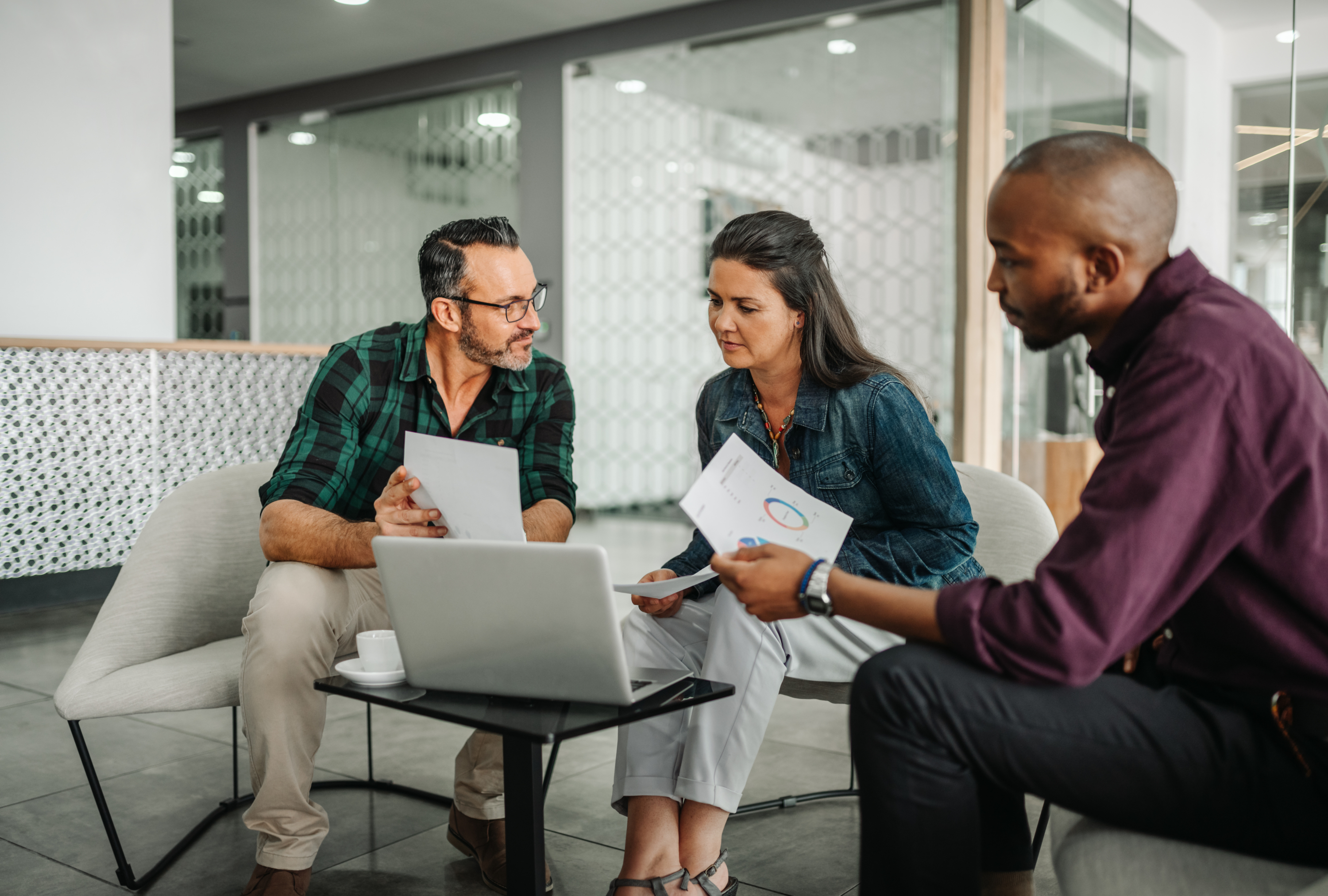 Three colleagues discuss reports and tasks during a meeting at the office.