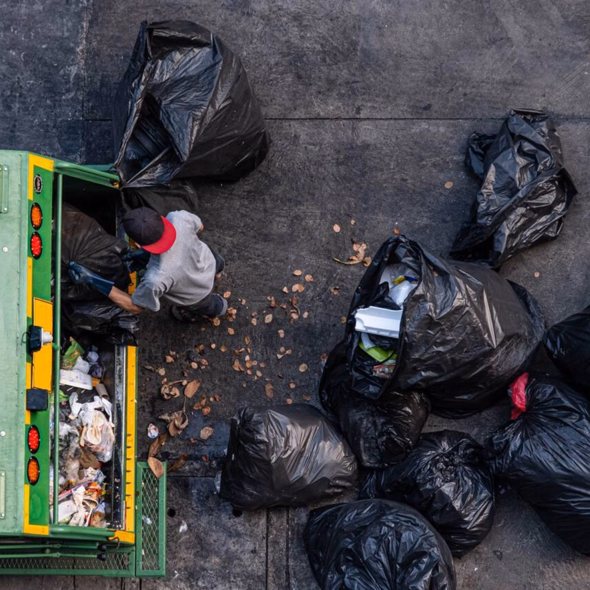 Véhicule de collecte des déchets entouré de sacs poubelles lors du traitement des déchets sur un terrain pavé.
