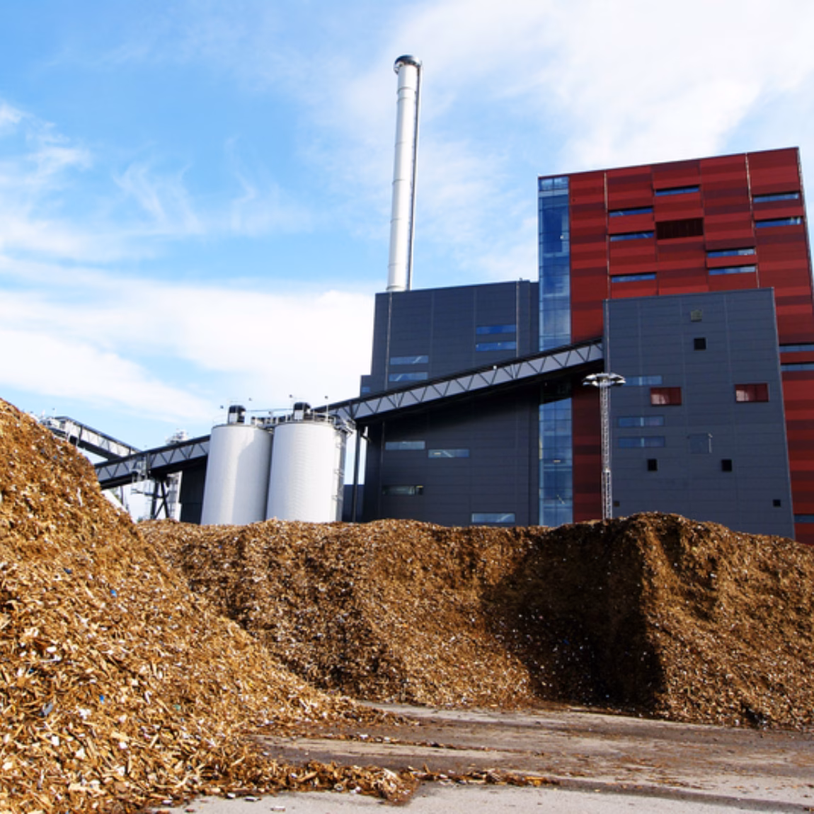 Biomassacentrale met grote hopen houtsnippers op een industrieterrein voor duurzame energieopwekking.